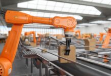 Must-Buy: 3 Robotics Stocks Beyond Tesla Now 2026! An articulated robotic arm is handling a package.